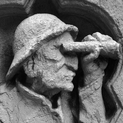 Detail of cement or stone cast or maybe carved sculpture of man in prfoile wearing a rain or sailing hat, maybe a helmet, looking to the right and holding up and looking through a telescope or binoculars